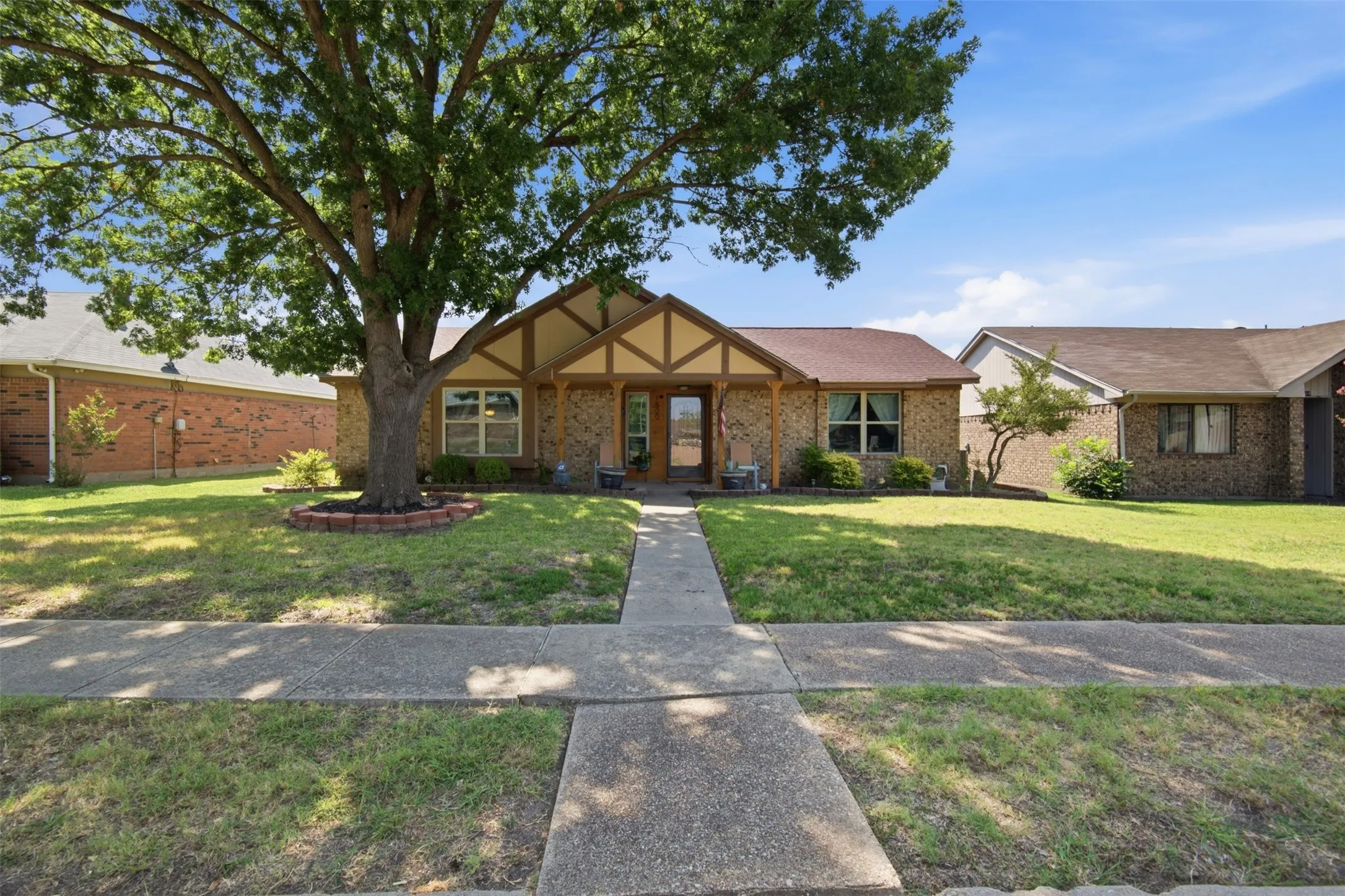 Brick facade residence with a prominent mature tree in the front yard