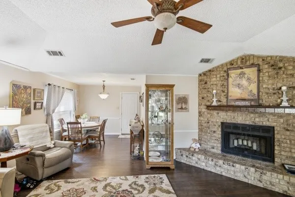 Spacious living area featuring wood-finish flooring, a brick fireplace, and a ceiling fan