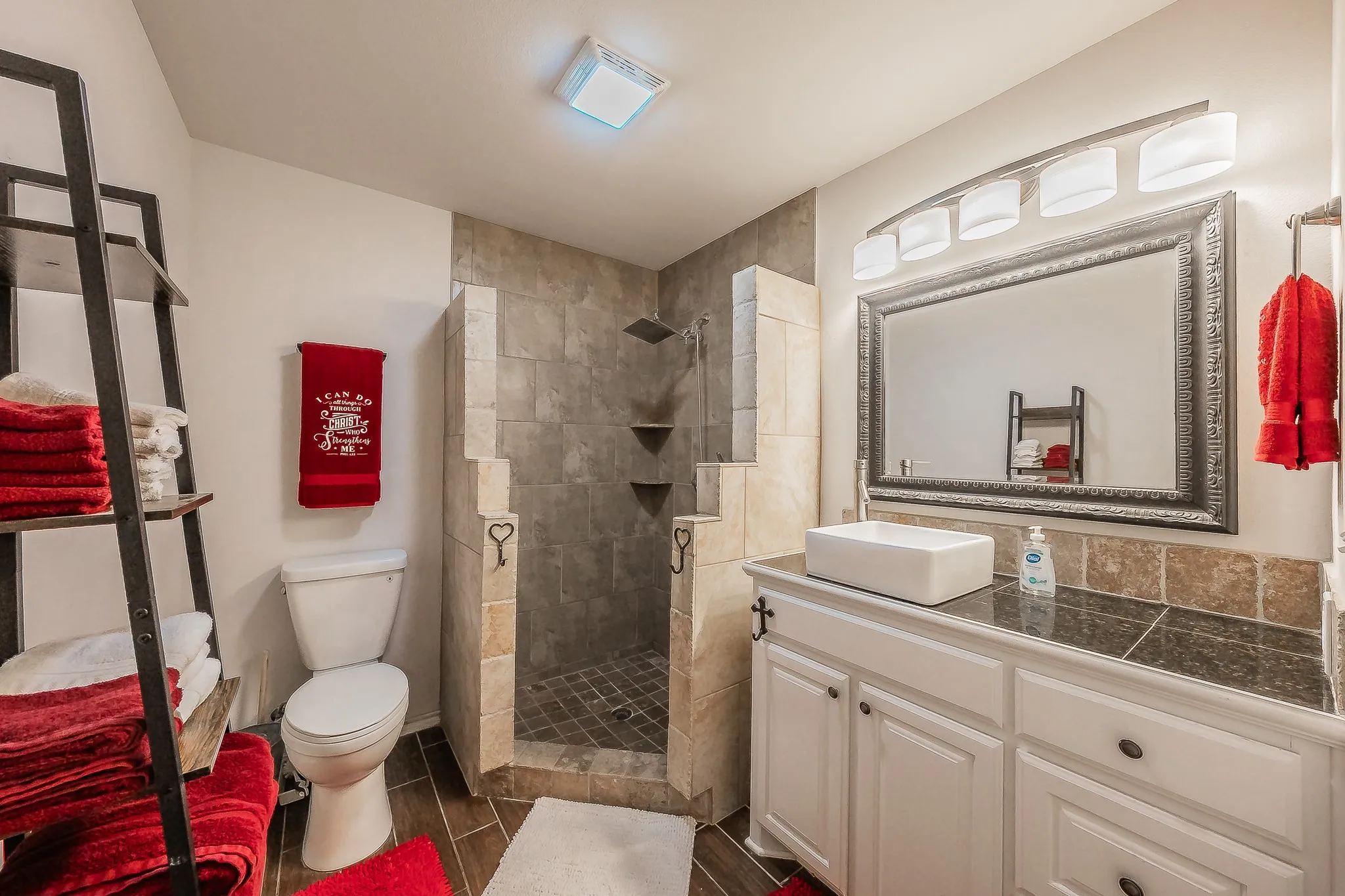 Mother In kaw Suite 0 batthroom featuring a walk-in shower with tile surround and built-in shelving, wood-finish flooring, a white vanity with vessel sink and dark countertop, and a large framed mirror with overhead lighting