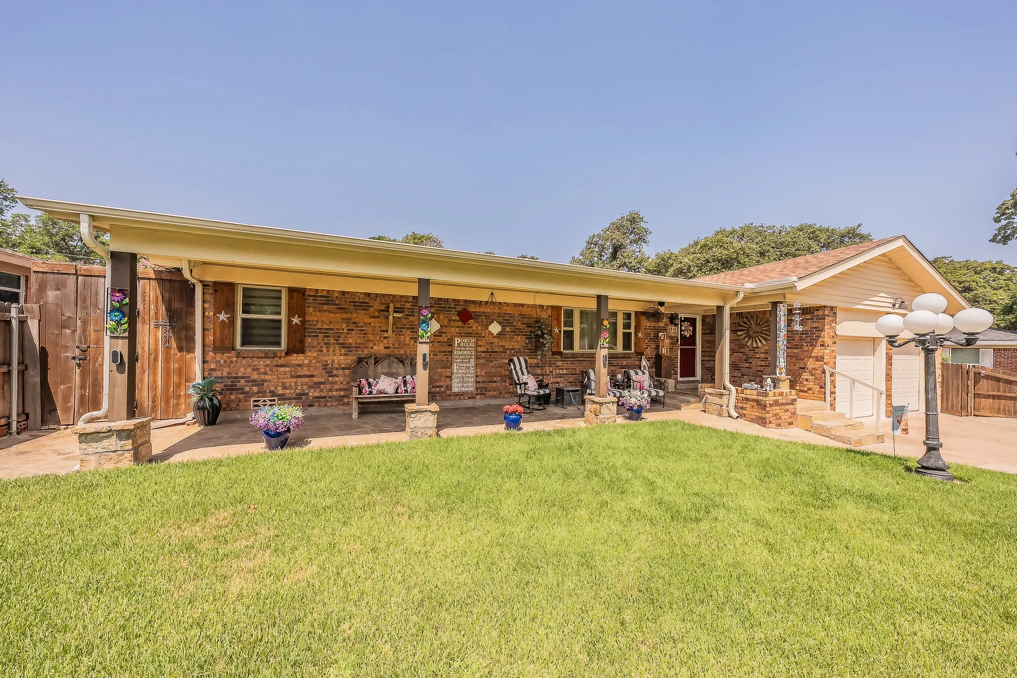 Brick-front residence with a covered front porch, an attached garage, a paved driveway, and a manicured lawn