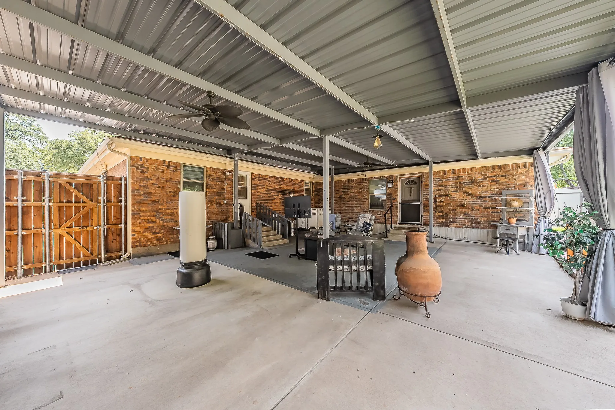 Expansive covered patio featuring a corrugated metal roof supported by metal beams, concrete flooring, and a ceiling fan