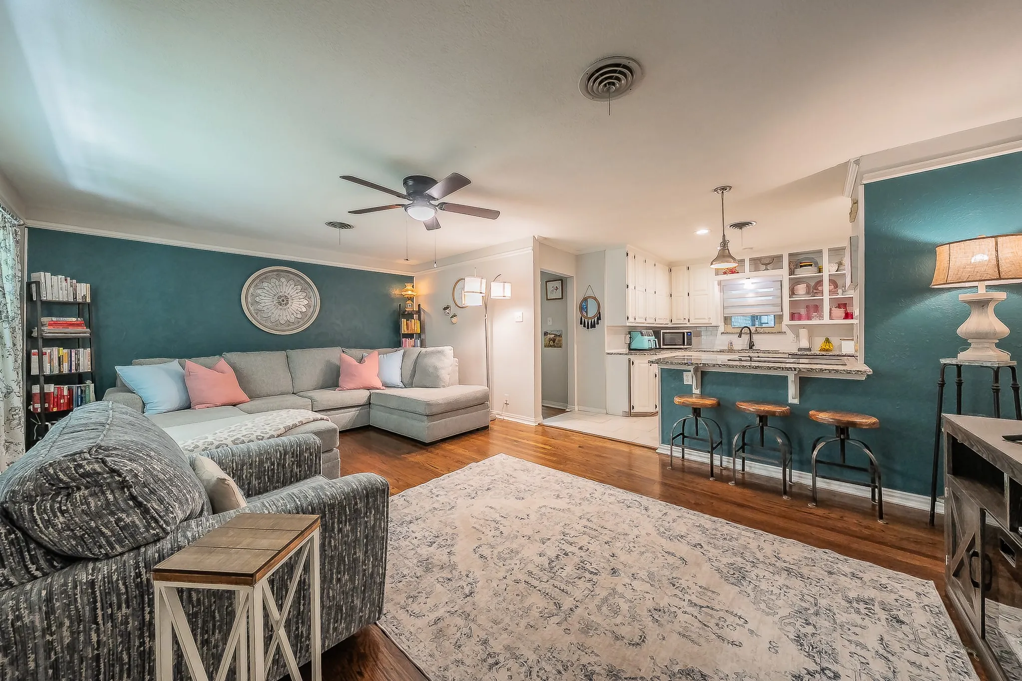 Open-concept living space featuring wood-finish flooring, a ceiling fan, and a kitchen pass-through with a breakfast bar