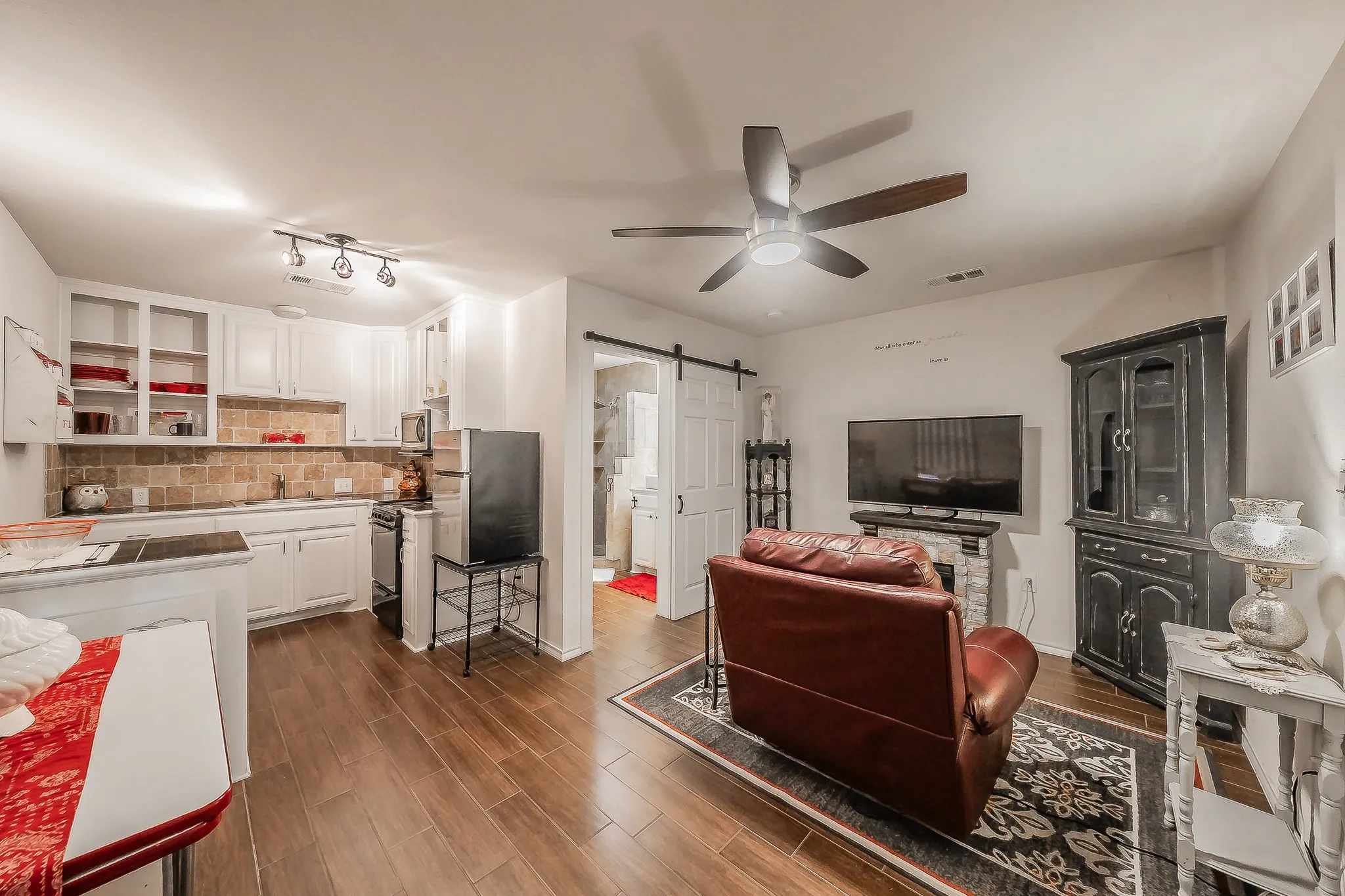Mother In Law Suite - Open-concept living area featuring wood-finish flooring, a contemporary ceiling fan, and a kitchen with white cabinetry and a stone tile backsplash