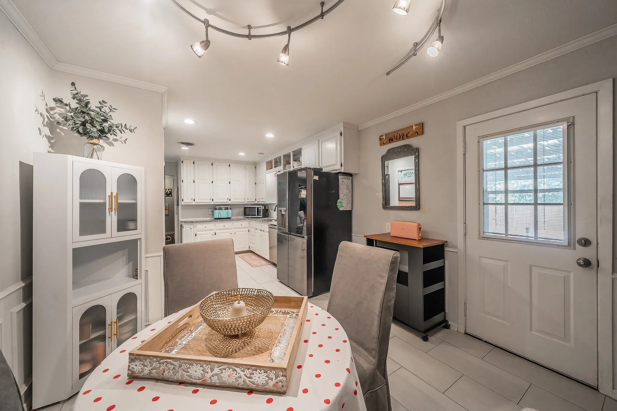 Bright kitchen and dining area featuring white cabinetry, track lighting, light tile flooring, and a glass-paneled door
