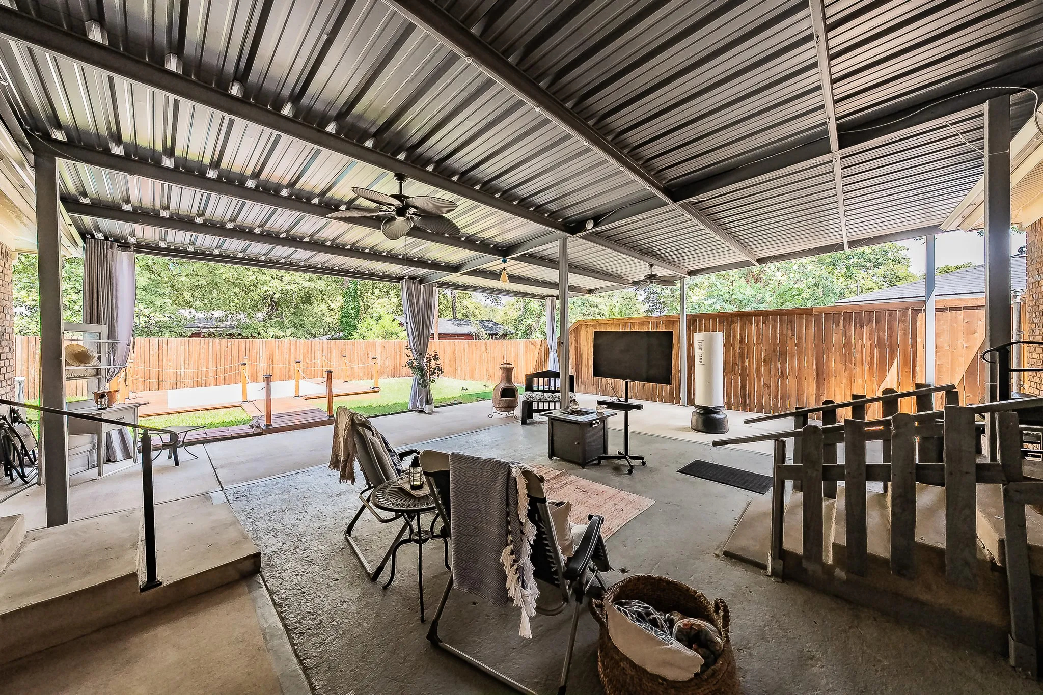 Expansive covered patio featuring a metal roof structure, ceiling fans, concrete flooring, and a wood privacy fence