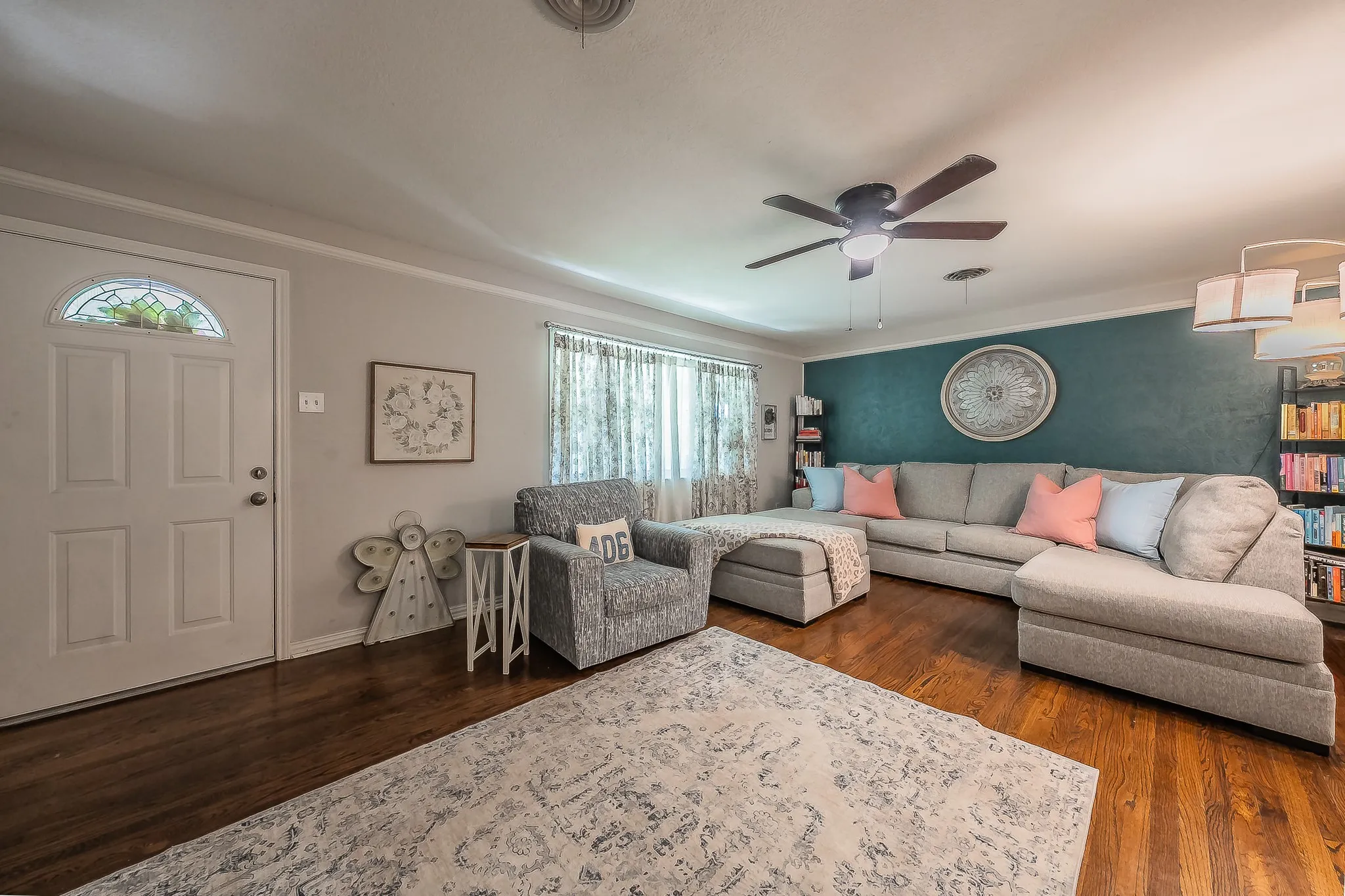 Living area featuring wood-finish flooring, a ceiling fan with integrated lighting, and a paneled entry door with a decorative glass insert