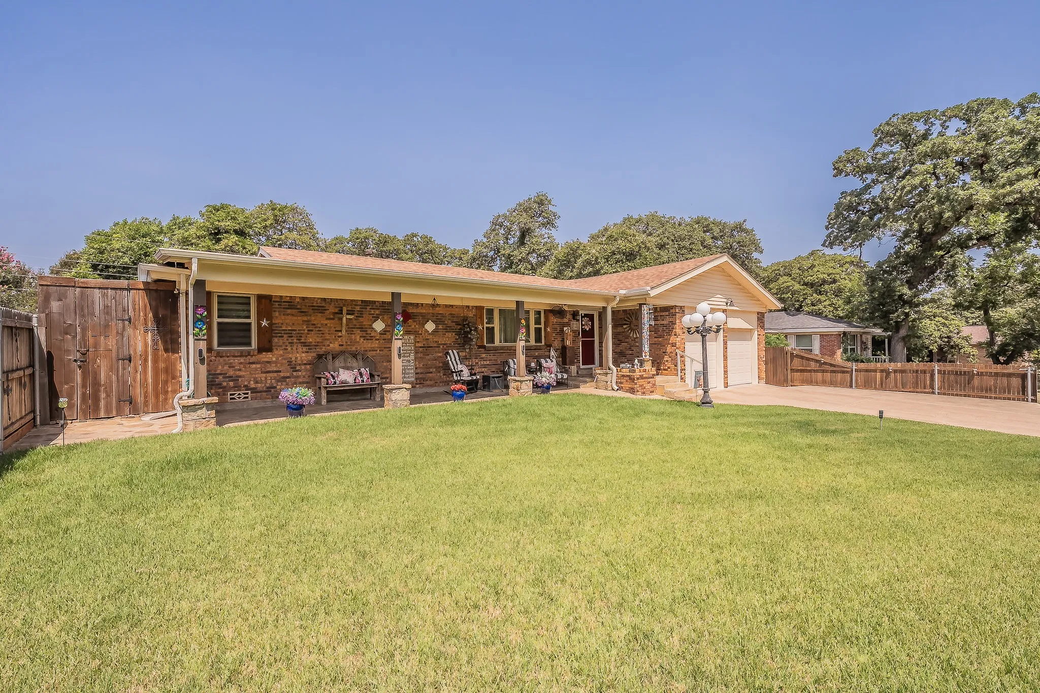 Brick facade ranch-style home featuring a covered front porch with stone-clad columns, a spacious front lawn, a paved driveway, and an attached two-car garage