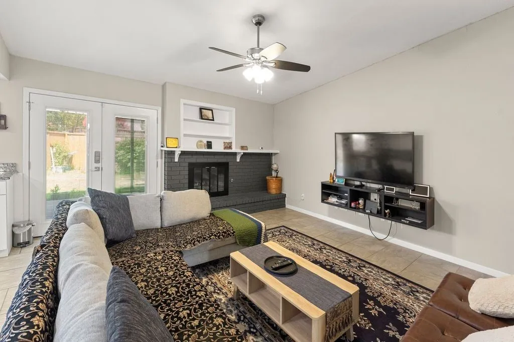Vaulted ceiling living area featuring a fireplace with built-in shelving, tile flooring, and double glass-paneled doors leading to the exterior