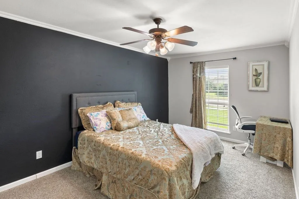 Bedroom featuring a dark accent wall, crown molding, and a ceiling fan with integrated lighting