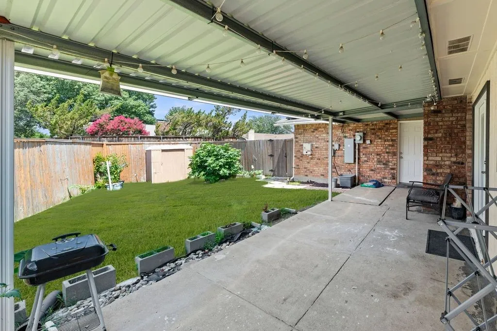 Covered concrete patio with string lighting, a red brick exterior wall, and a rear door