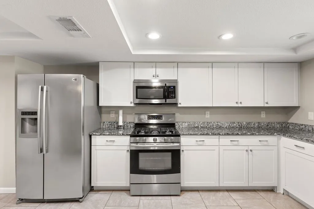 Modern kitchen featuring white cabinetry, stainless steel appliances, granite countertops, and recessed lighting