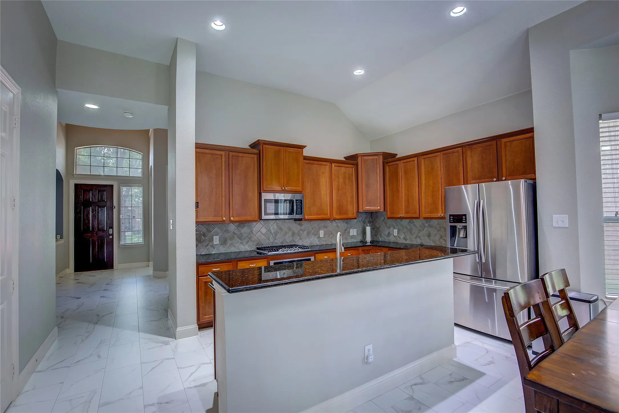 Kitchen with tasteful backsplash, light tile patterned floors, dark stone counters, stainless steel appliances, and a center island with sink