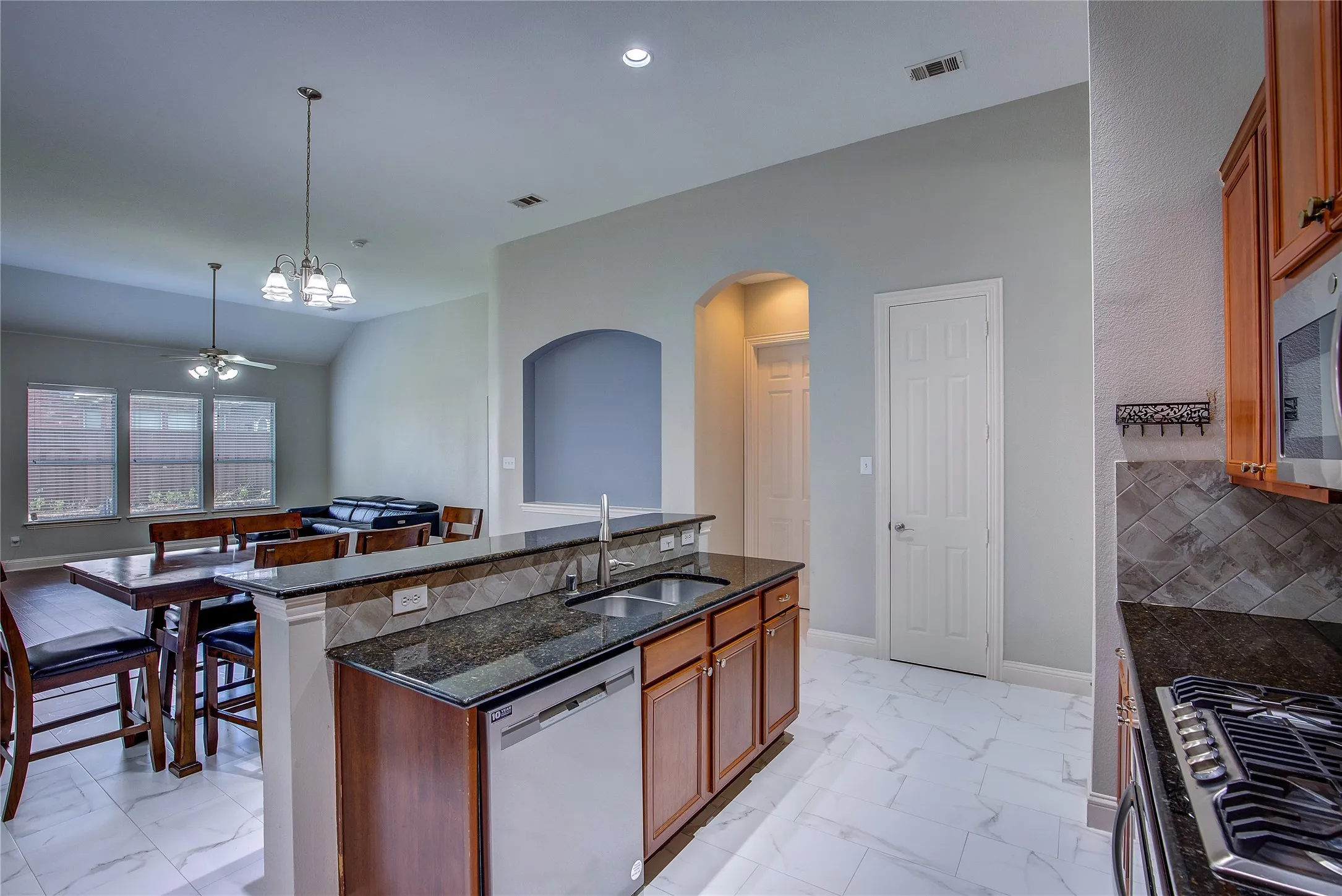 Kitchen featuring dark stone countertops, a center island with sink, backsplash, appliances with stainless steel finishes, and sink