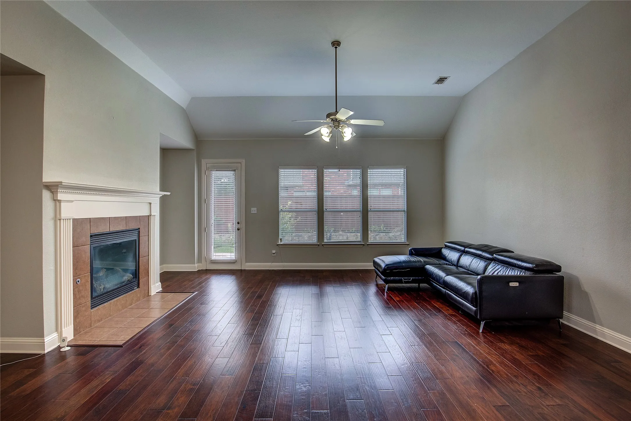 Living room with vaulted ceiling, a tile fireplace, ceiling fan, and hardwood / wood-style floors