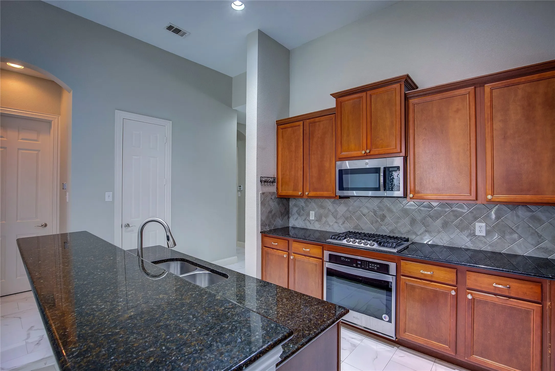 Kitchen with backsplash, appliances with stainless steel finishes, a kitchen island with sink, and light tile patterned floors
