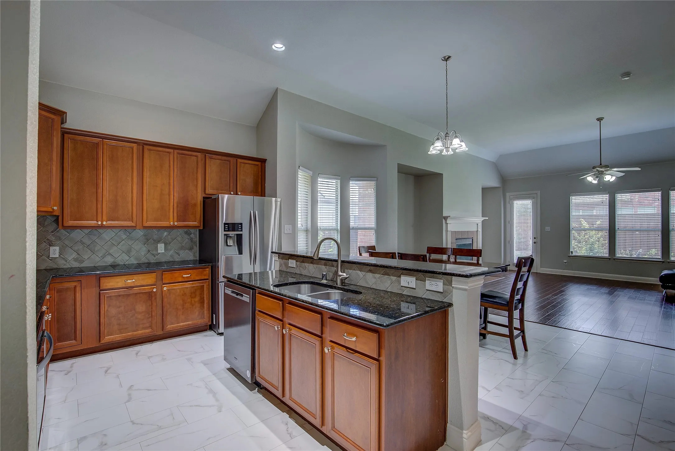Kitchen featuring decorative backsplash, light tile patterned floors, ceiling fan with notable chandelier, and a kitchen island with sink