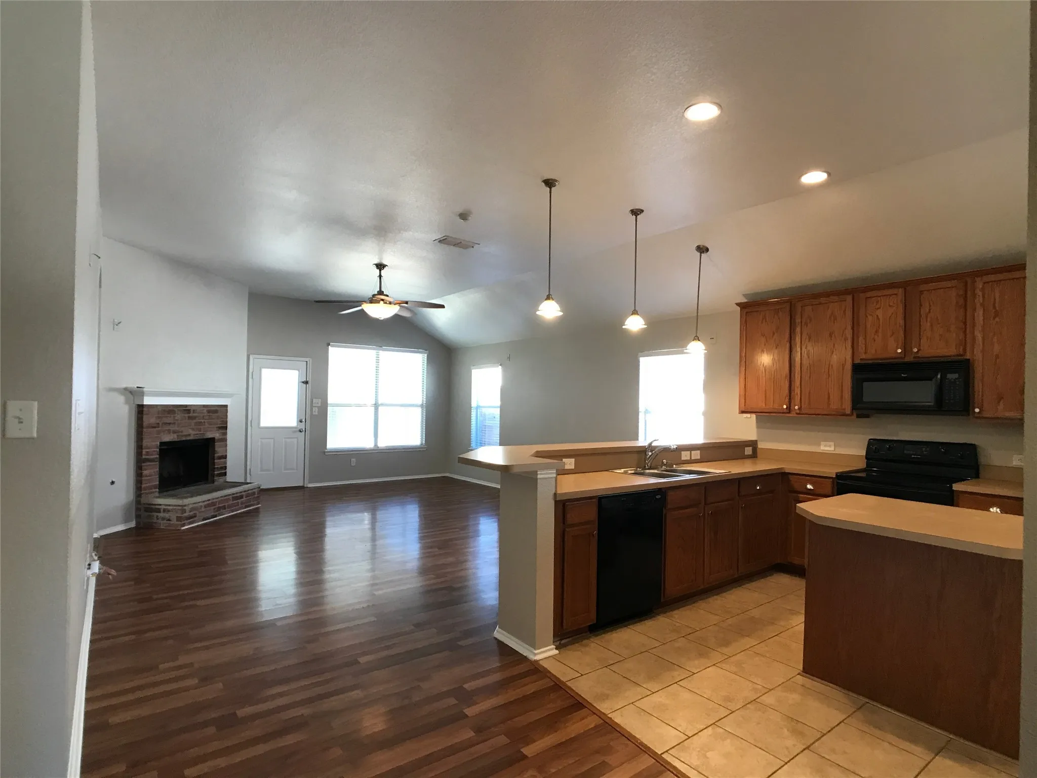 Open-concept kitchen and living area featuring a brick fireplace, vaulted ceilings, and wood-finish flooring