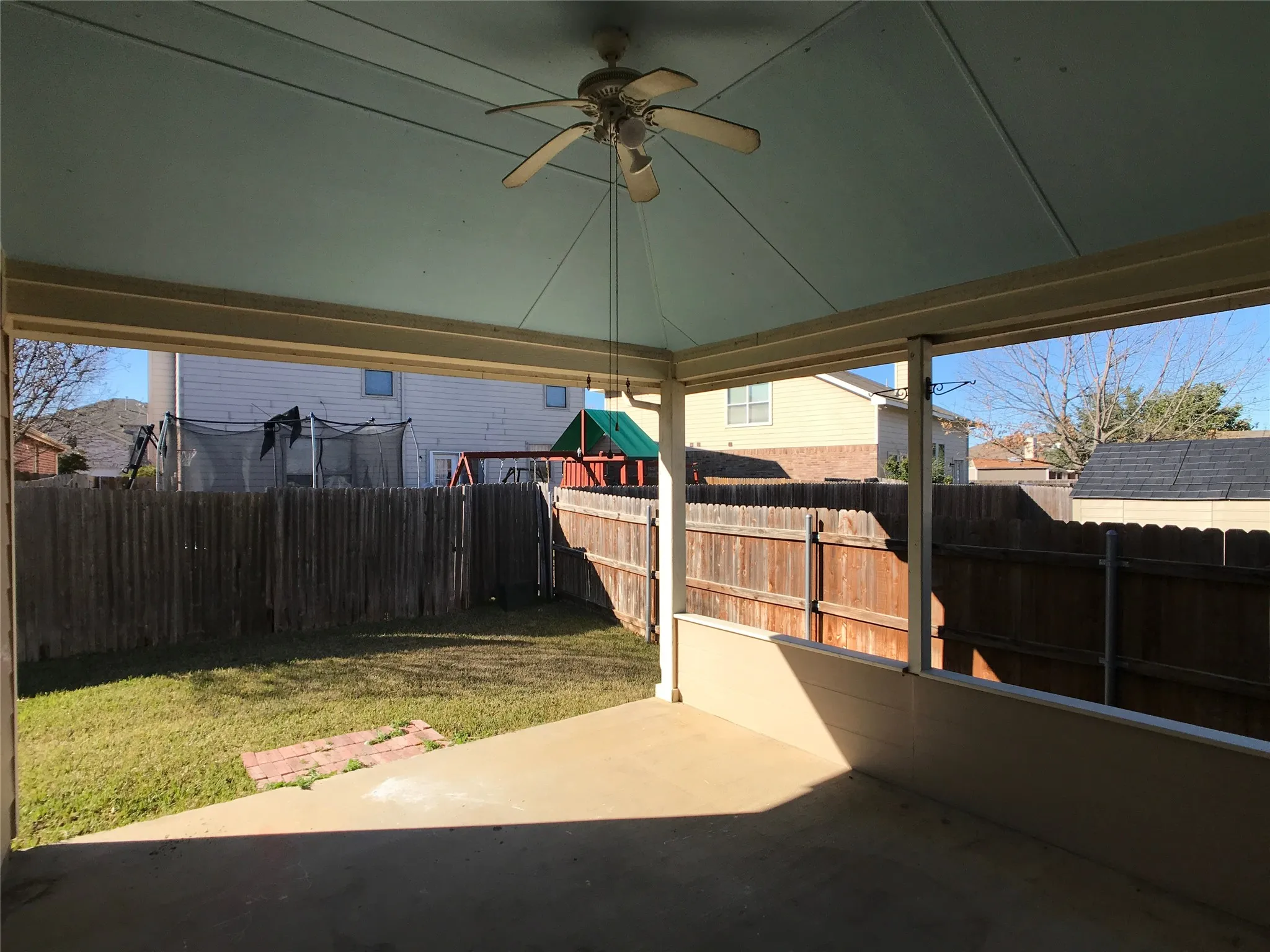 Covered patio with a ceiling fan, concrete flooring, and a partial privacy wall