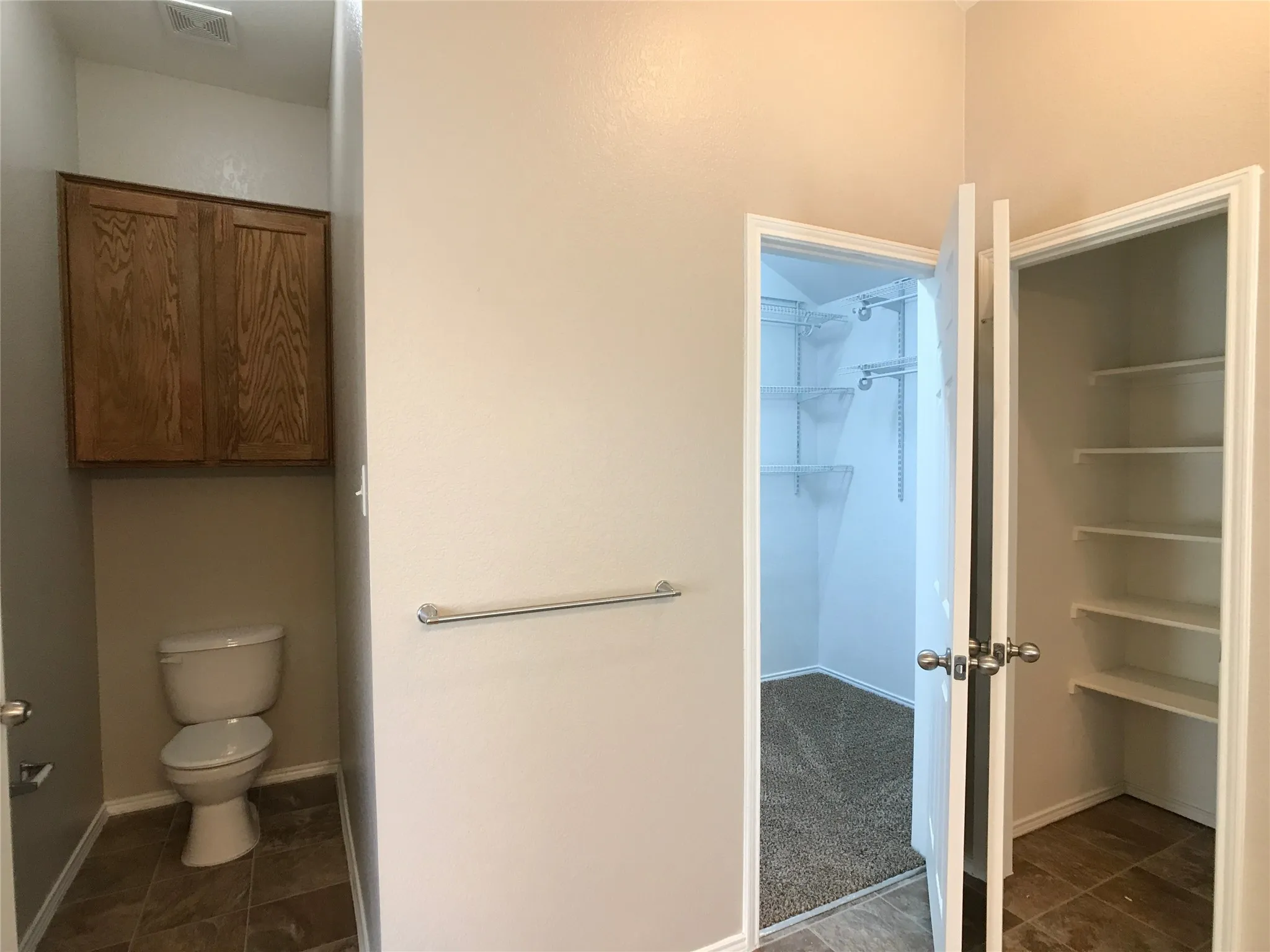 Powder room featuring a toilet with an overhead wood-finish cabinet and tile flooring