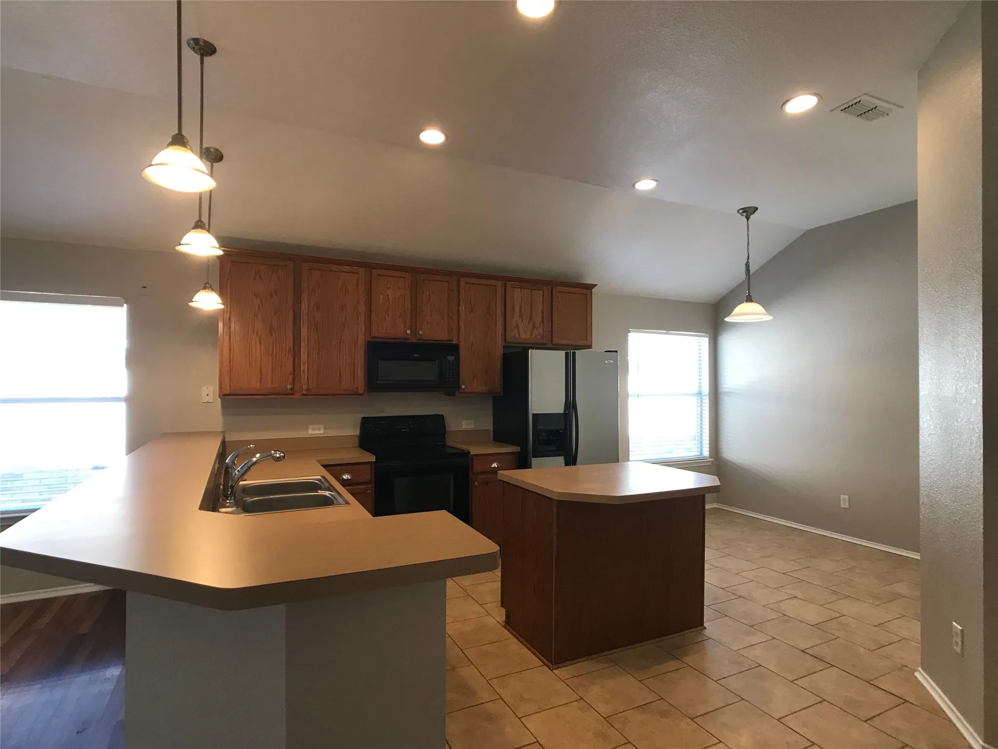 Open-concept kitchen featuring wood cabinetry, stainless steel refrigerator, and recessed lighting