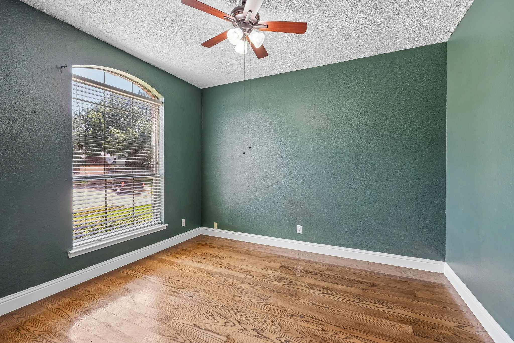 Room featuring wood-finish flooring, a prominent arched window with blinds, and white baseboards