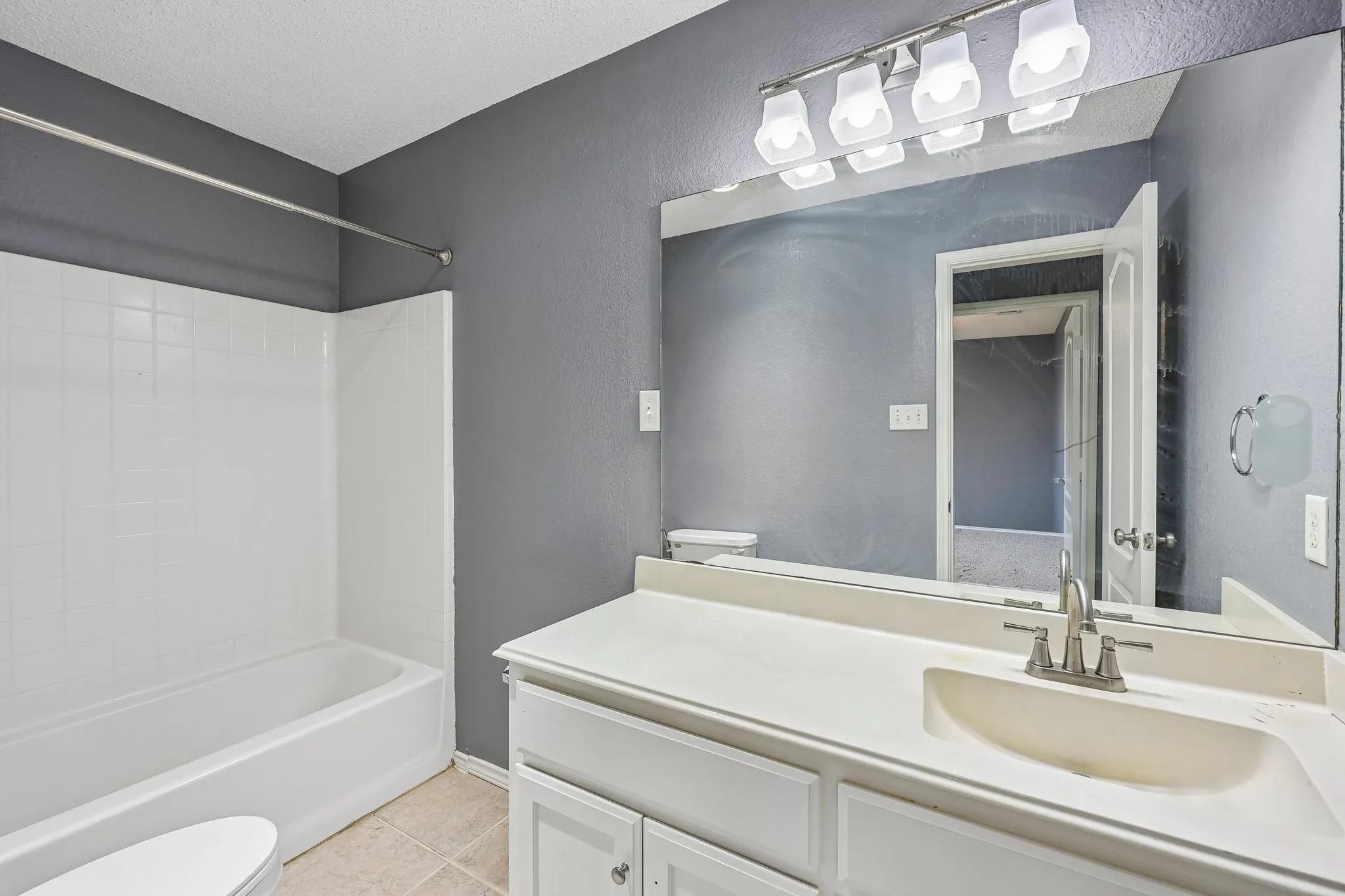 Full bathroom featuring a white tub and shower surround, a white vanity with integrated sink, a large wall-mounted mirror, and tile flooring