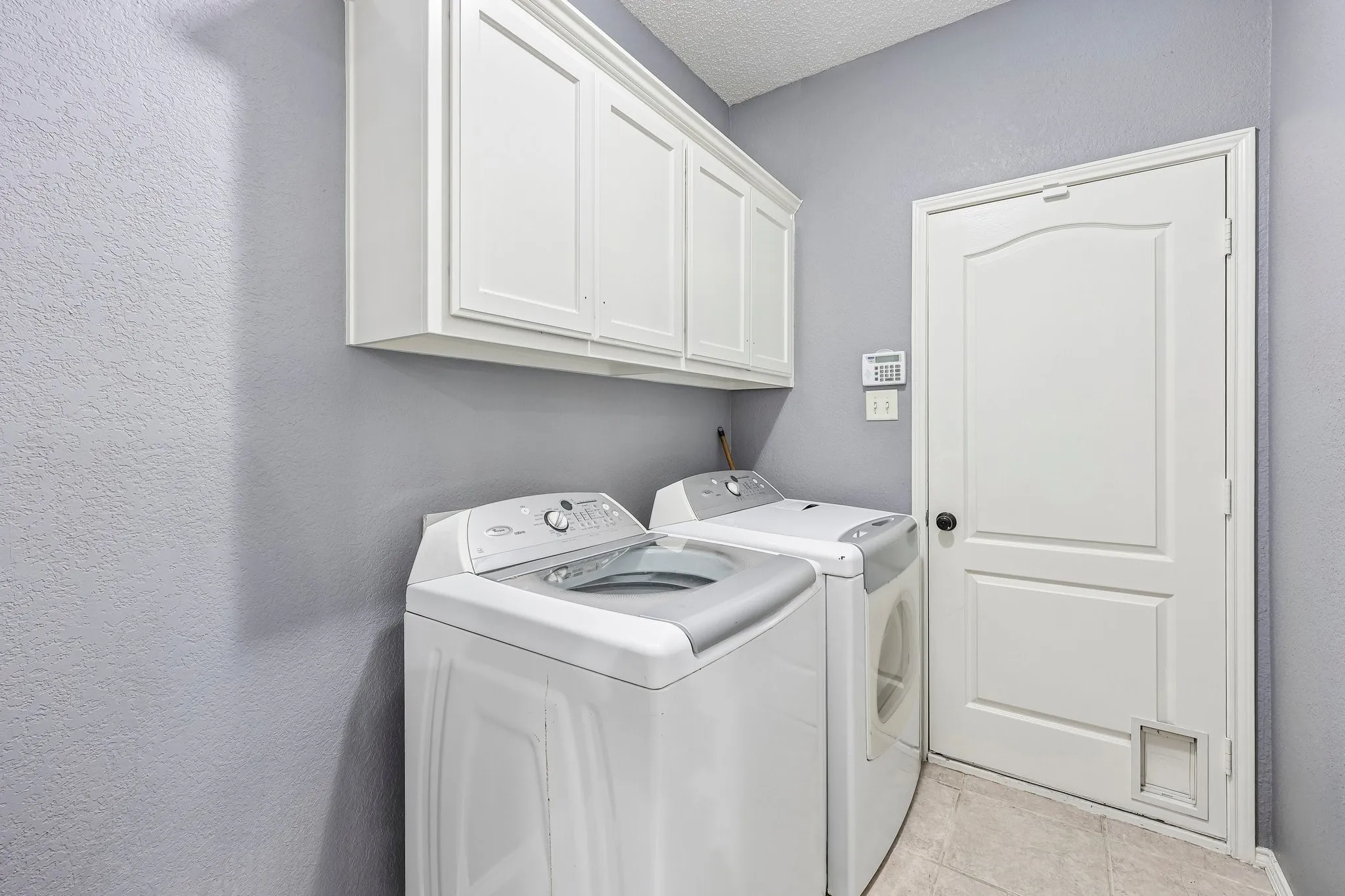 Laundry area featuring upper cabinetry, a white paneled door, and neutral tile flooring