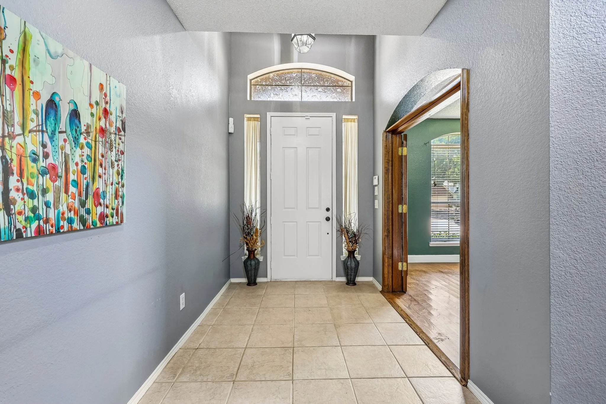 Entryway featuring a paneled door with an arched transom window, ceramic tile flooring, and an arched doorway leading to a room with wood-finish flooring