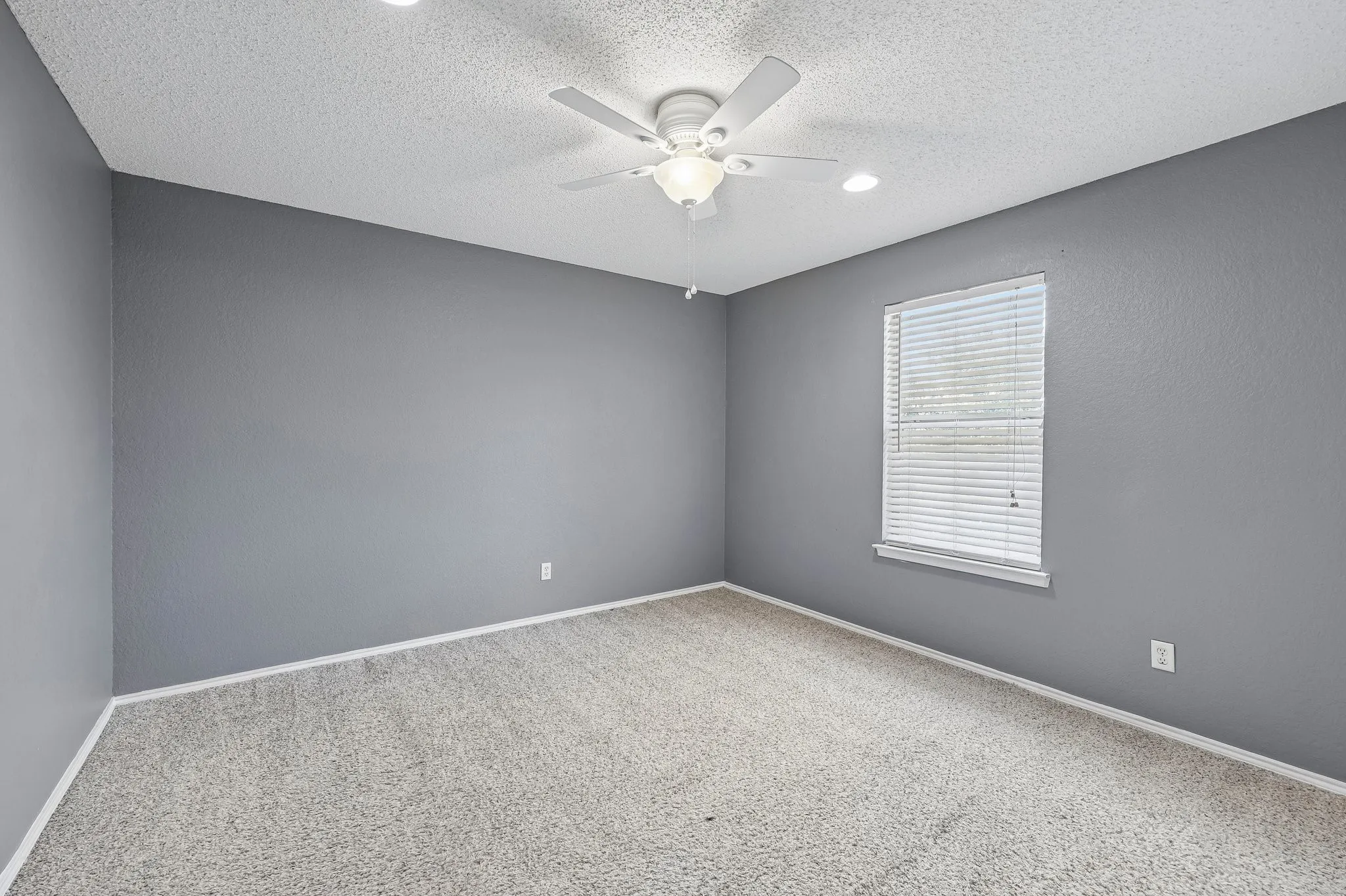Spacious room featuring textured gray walls, textured white ceilings, recessed lighting, and a ceiling fan with integrated lighting