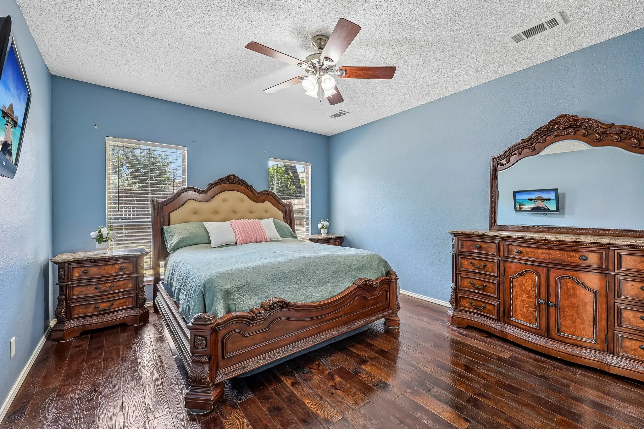Spacious room featuring wood-finish flooring, a ceiling fan with light fixture, and two windows with blinds