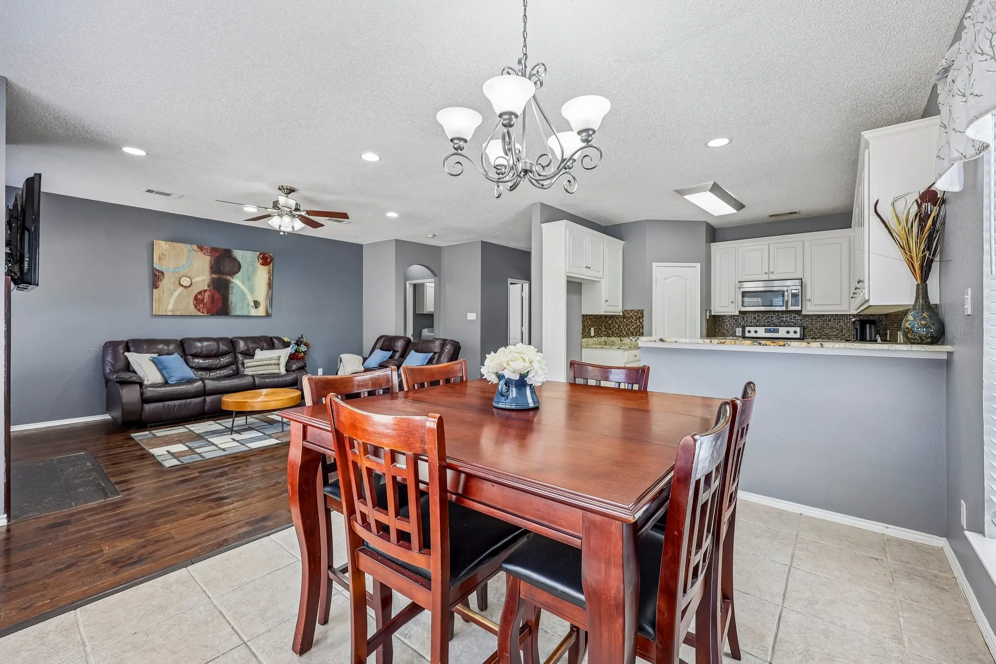 Open-concept living area featuring a formal dining space with a chandelier, tile flooring, and wood-finish flooring in the living room