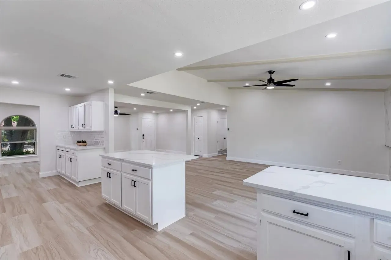 Bright and spacious kitchen featuring white cabinetry with hardware accents, a large center island with seating counter, stainless steel appliances, and wood-finish flooring throughout