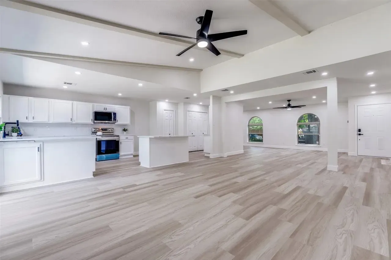 Expansive open-concept living area featuring light wood-finish flooring, recessed lighting, and exposed ceiling beams