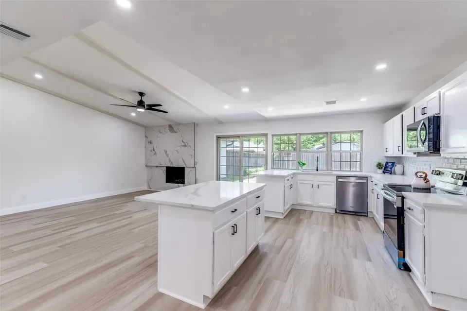Bright, open-concept kitchen featuring white cabinetry with hardware accents, stainless steel appliances including a gas range and refrigerator, quartz countertops, and a substantial island with seating