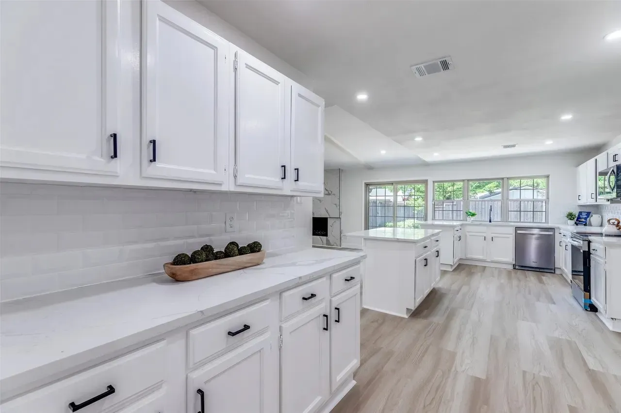Bright, modern kitchen featuring crisp white cabinetry with black hardware, white subway tile backsplash, and stainless steel appliances
