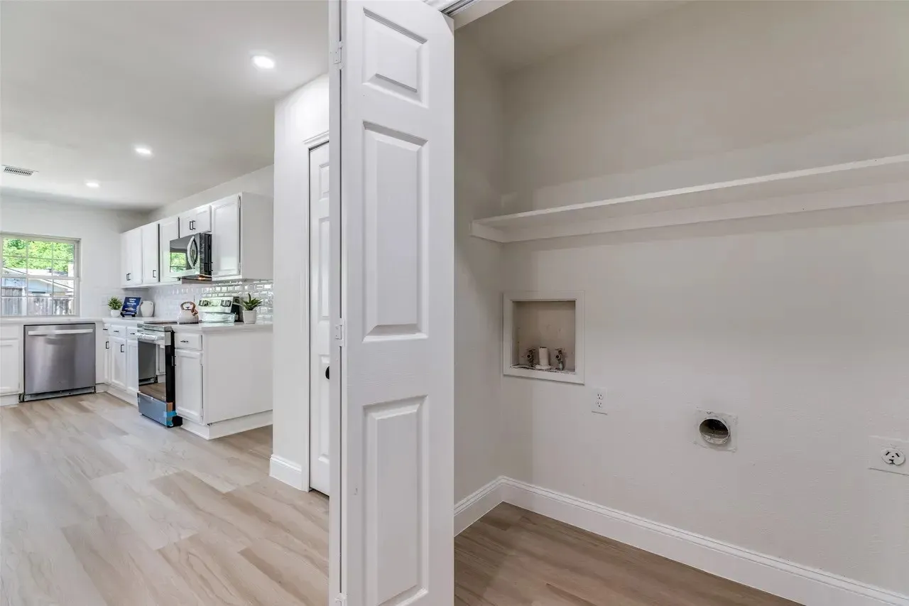 Laundry area with shelving, integrated utility connections, and wood-finish flooring