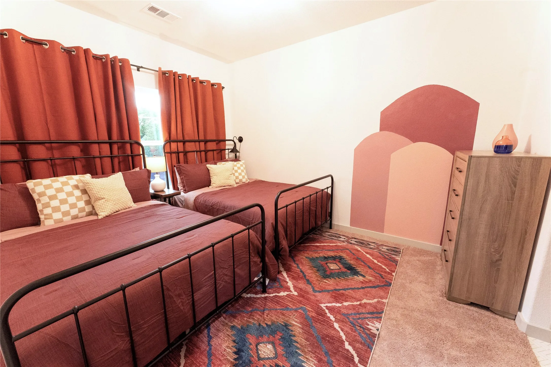 Dual-bedroom layout featuring wrought-iron bed frames with coordinating rust-toned bedding, decorative throw pillows, and geometric patterned area rugs