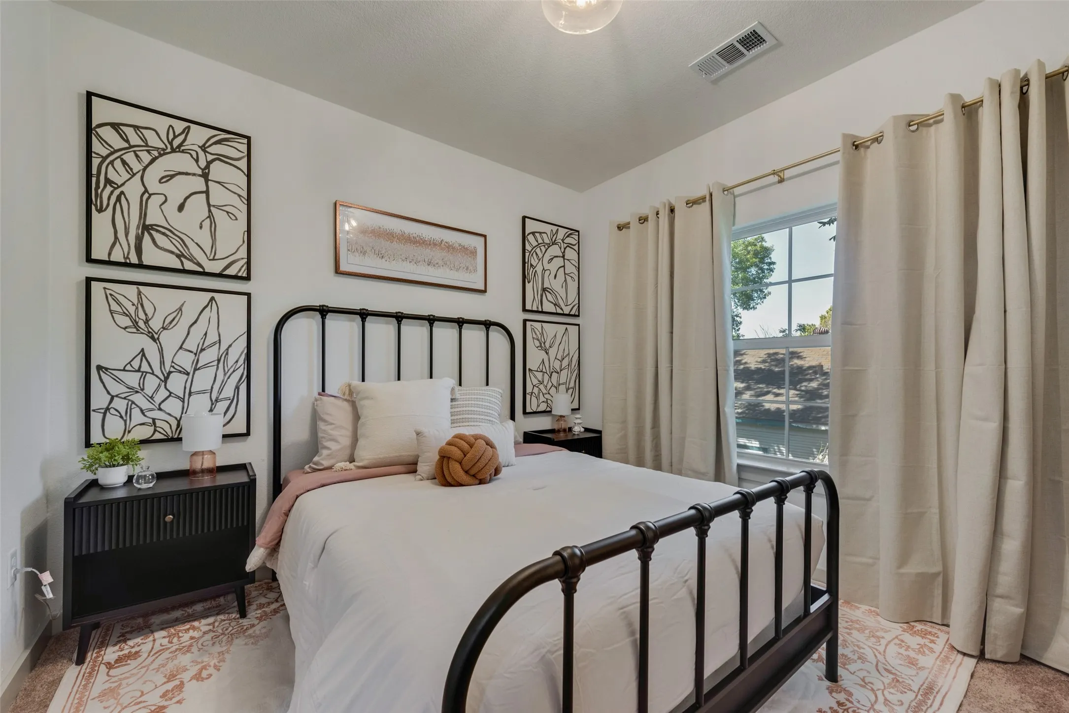 Bright bedroom showcasing a black metal bed frame, white bedding, and neutral upholstered headboard accents
