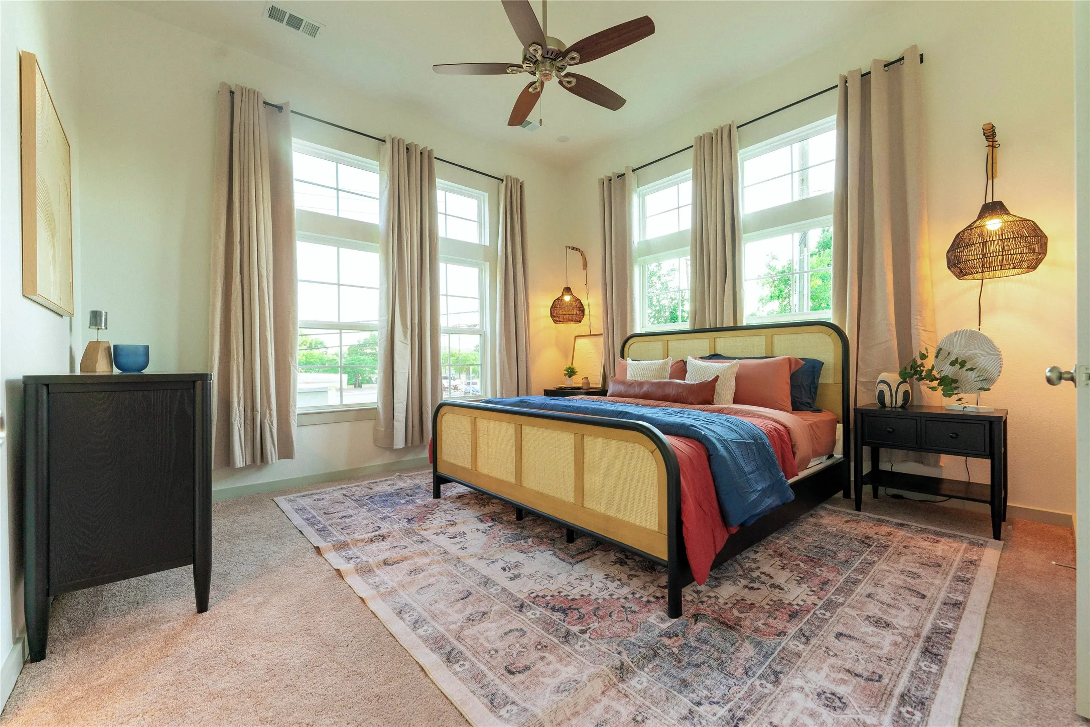 Spacious bedroom featuring multiple double-hung windows, a ceiling fan with light fixture, light-colored carpeting, and neutral wall paint