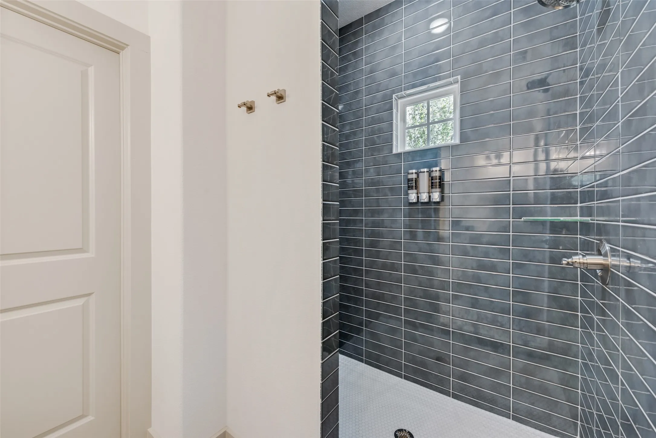 Modern bathroom featuring a frameless glass shower enclosure with sleek gray linear tile walls, a white subway tile base, recessed shelving for toiletries, and brushed nickel​​‌​​​​‌​​‌‌​‌‌​​​‌‌​‌​‌​‌​​​‌​​ fixtures