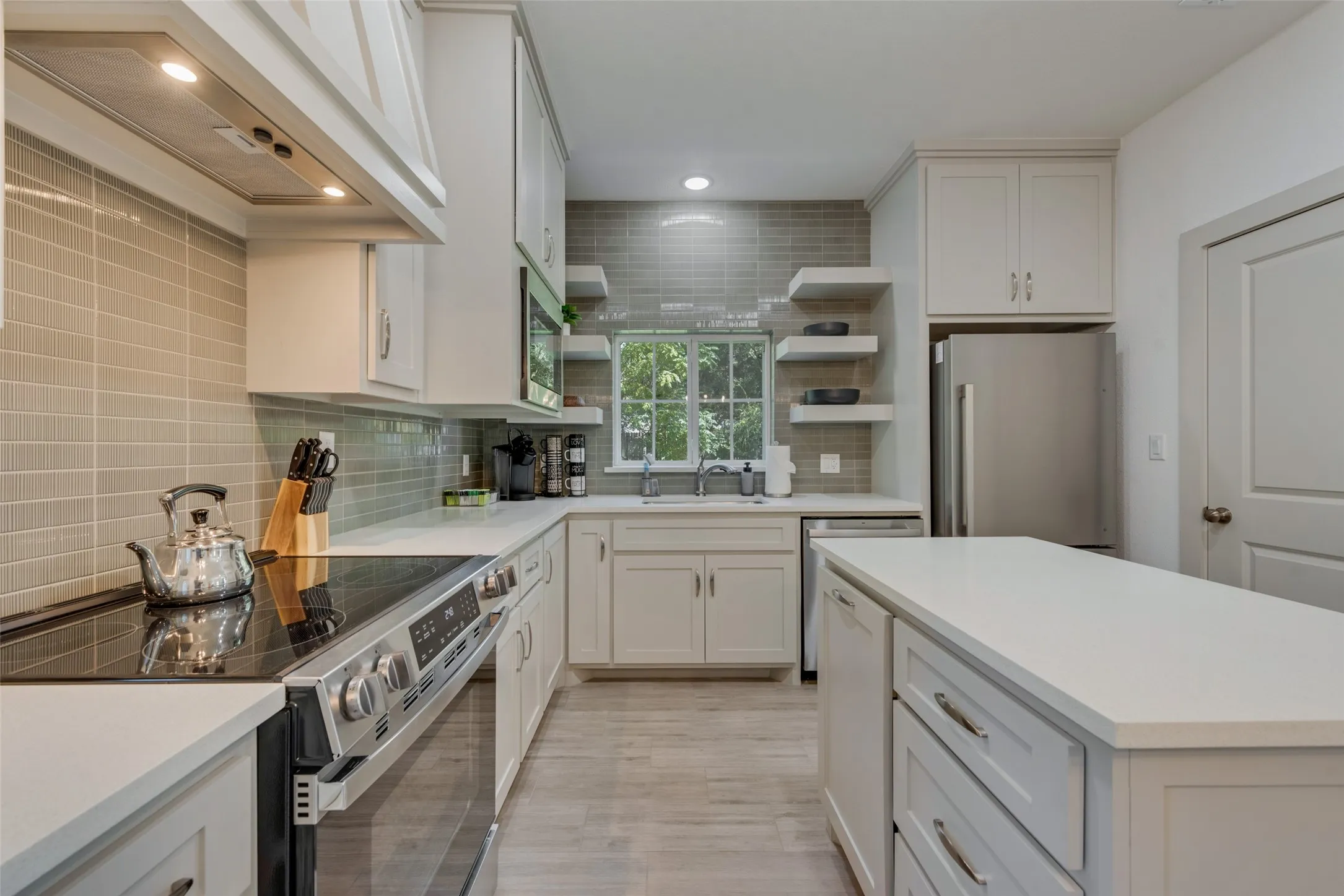 Modern kitchen featuring light cabinetry, stainless steel appliances, a center island, light wood-finish flooring, and a subway tile backsplash