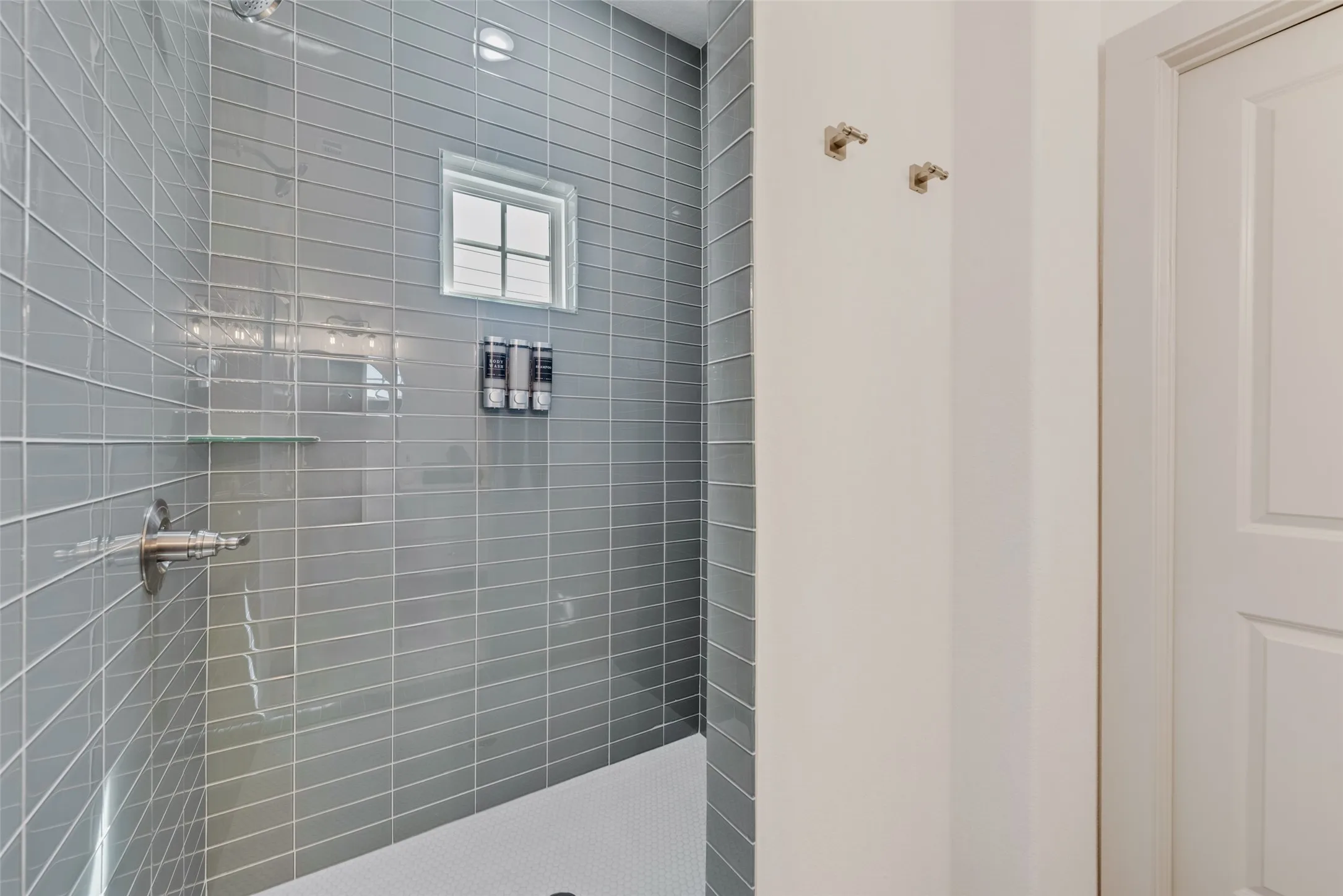 Modern walk-in shower featuring gray subway tile walls, frameless glass enclosure, chrome fixtures, and a recessed niche for toiletries