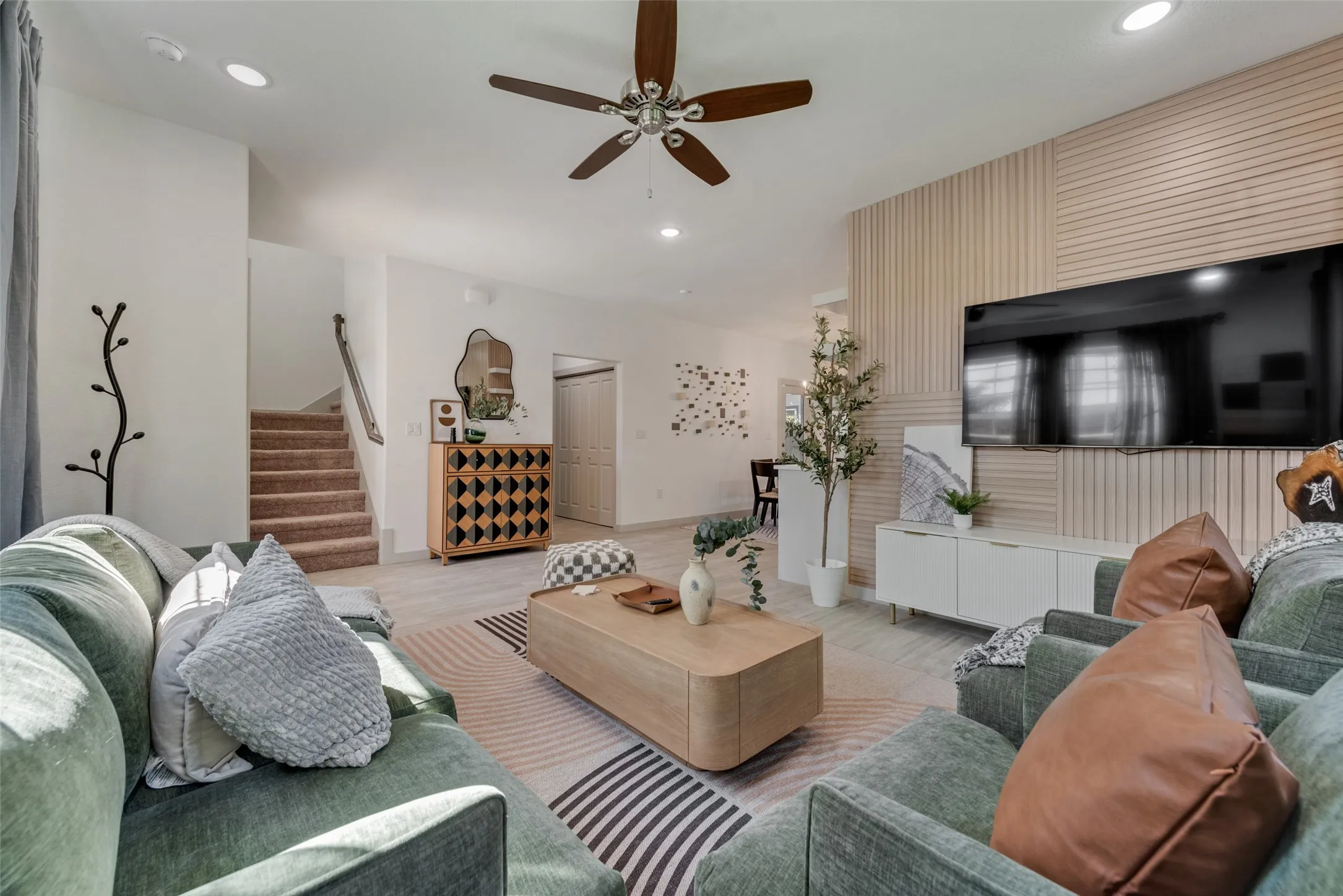 Open-concept living area featuring a wood-finish plank accent wall, recessed ceiling lighting, and a ceiling fan