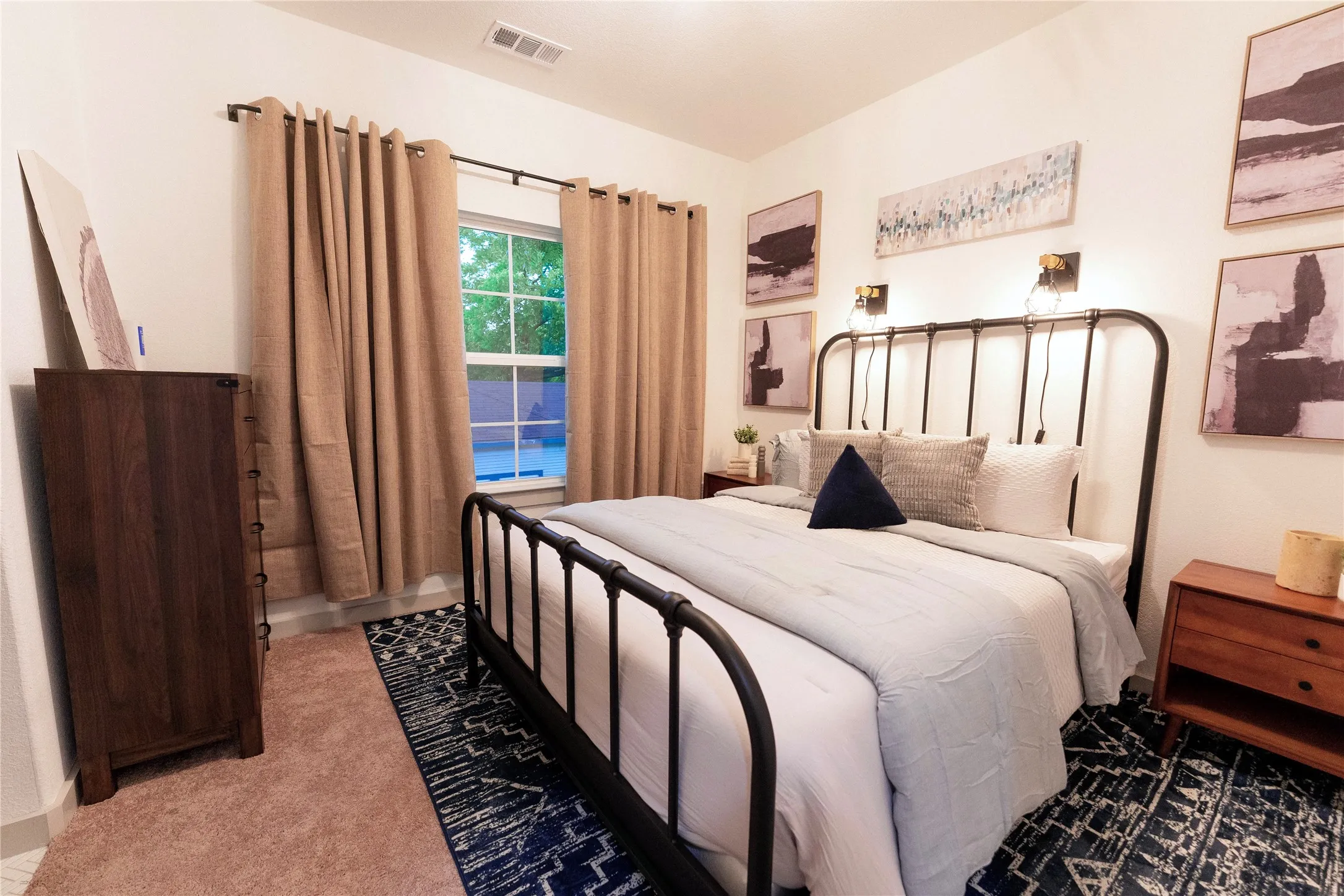 Spacious bedroom featuring a wrought iron bed frame, neutral bedding, and soft natural light from a large window dressed with tan grommet curtains