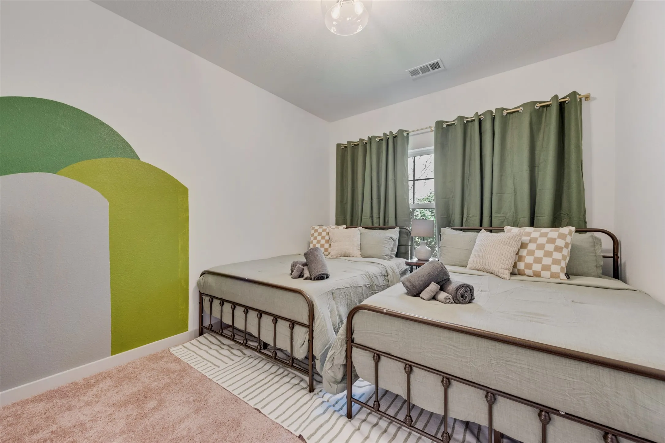 Dual-bed bedroom featuring metal frame beds with upholstered headboards, striped area rug, and grommet-top curtain panels in sage green