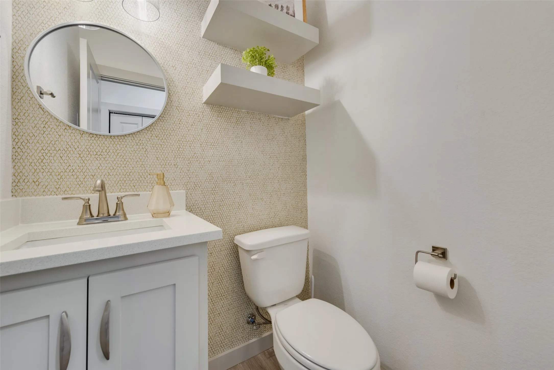 Elegant powder room featuring a gray vanity with white countertop, brushed gold three-hole faucet, and chrome-framed round mirror