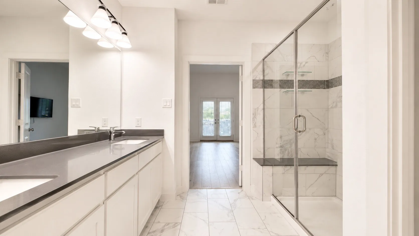 Bathroom featuring marble-look tile flooring, a dual vanity with a gray countertop, an expansive mirror, and a glass-enclosed shower with a built-in bench