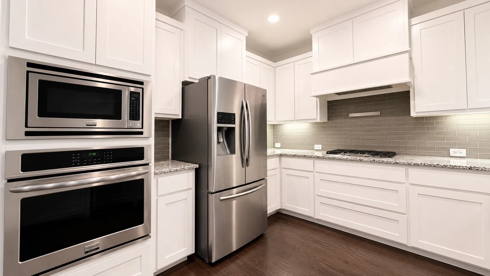 Chef's kitchen featuring white shaker cabinetry, stainless steel French-door refrigerator, dual wall-mounted ovens with black glass fronts, under-cabinet microwave, gas cooktop, subway tile backsplash, granite countertops, and wood-finish flooring throughout