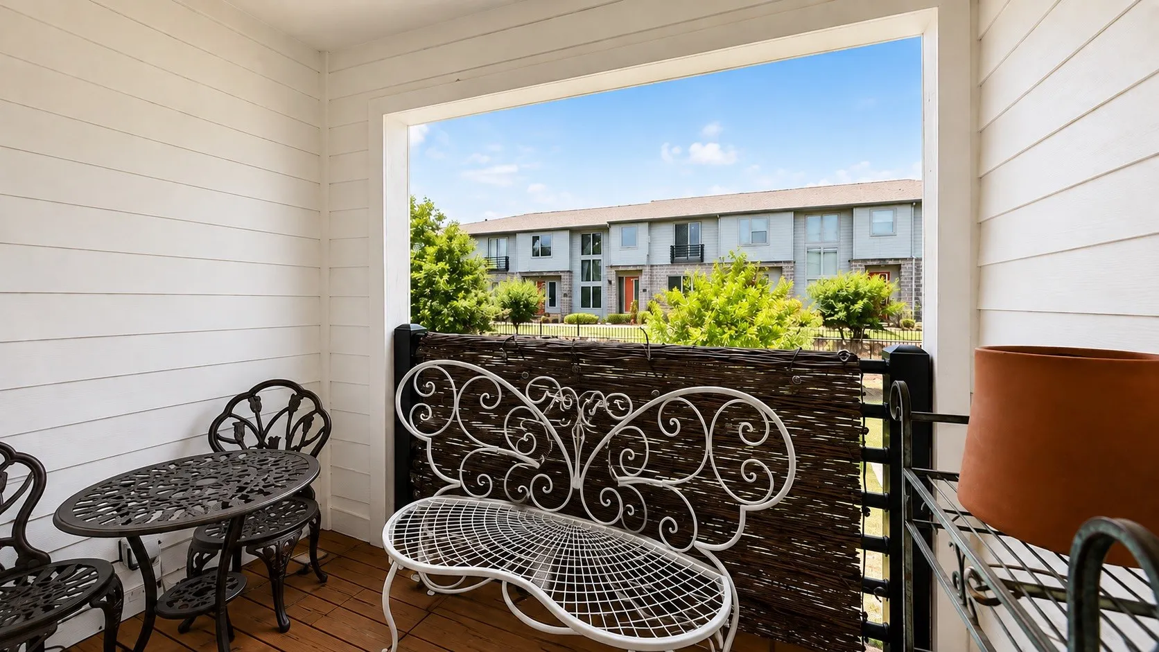 Private balcony featuring decorative wrought-iron railing, wood-finish flooring, and shiplap wall detailing