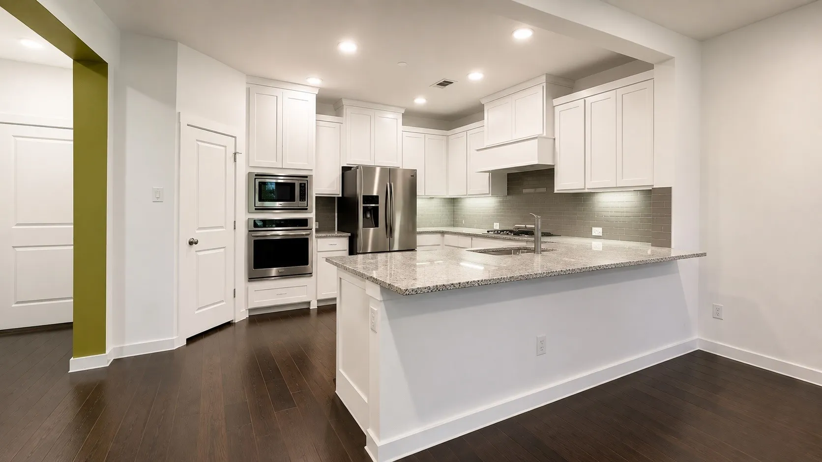 Gourmet kitchen featuring white cabinetry, stainless steel appliances including dual wall ovens, quartz countertops, and a large center island with waterfall edge